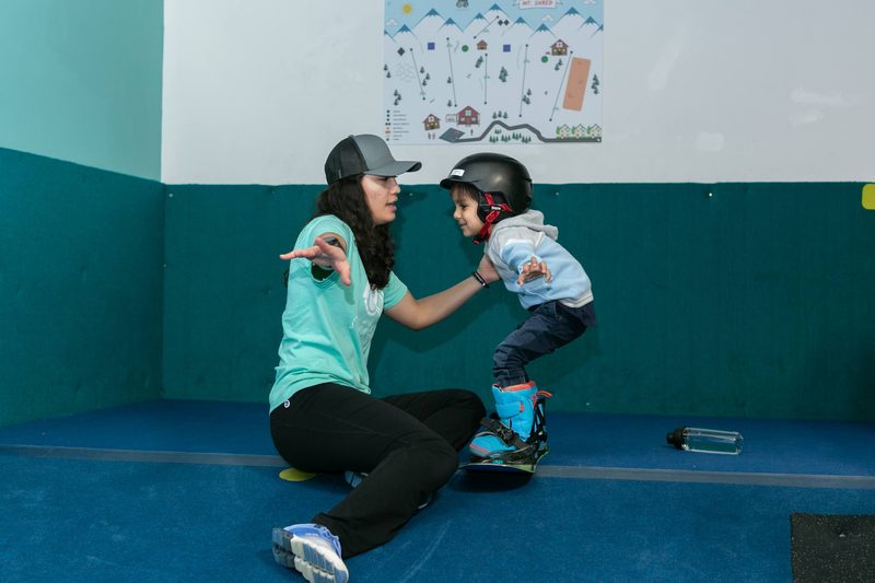 A coach kneeling on the slope with a toddler learning to stand on a board