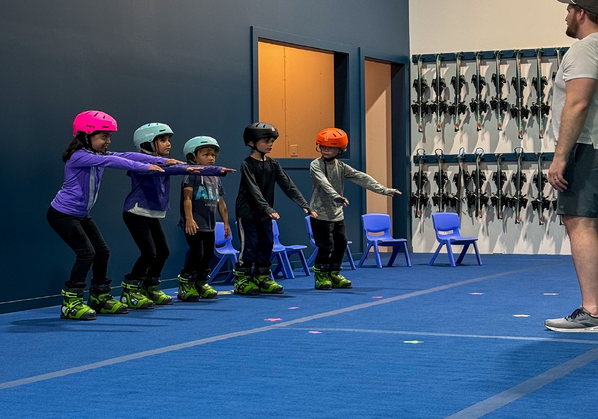 Group of kids in skill stance on the indoor slope, instructor coaching